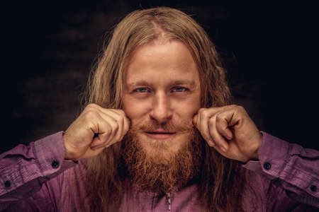 Portrait of a happy redhead hermit with long hair and beard in a purple shirt. Isolated on dark background.の写真素材