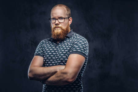 Portrait of a redhead bearded male dressed in a t-shirt posing with crossed arms. Isolated on dark textured background.の写真素材