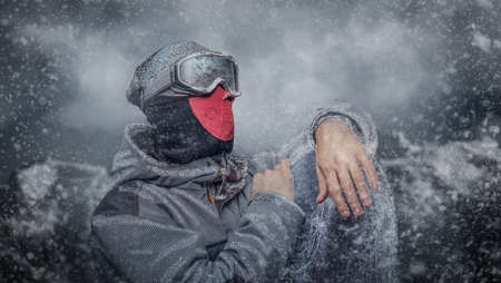 Portrait of a snowboarder dressed in a full protective gear for extream snowboarding posing with snowboard against the background of mountainsの写真素材