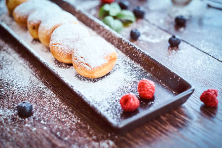 Close-up photo of a set donuts sprinkled with powdered sugar on a black long plate with raspberry...