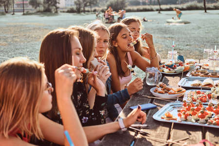 Group of happy girlfriends eating at the table together celebrating a birthday at the outdoor park.