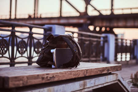 Close-up photo of a backpack and a skateboard that lie on a bench on the embankment during a beautiful sunset.の写真素材