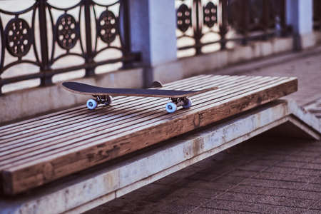Close-up photo of a skateboard that standing on a bench on the embankment during a beautiful sunset.