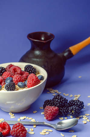 Healthy breakfast. White plate with oatmeal strewn and different berries on a blue background.