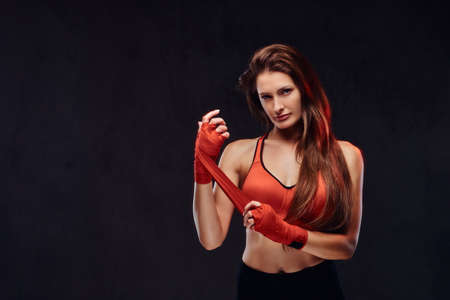 Portrait of a beautiful brunette female boxer in sports bra bandages her hands. Isolated on a dark textured background.の写真素材