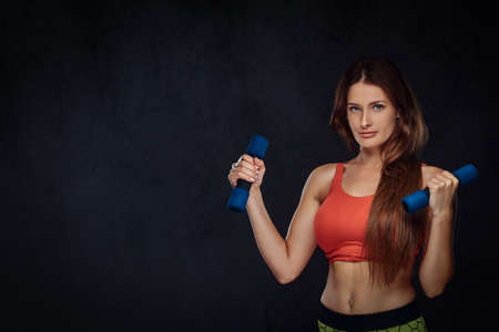 Fitness woman dressed in sports bra doing exercise with dumbbells. Isolated on dark textured...