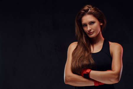Portrait of a beautiful sportive female boxer in sportswear and bandaged hands, posing with crossed...