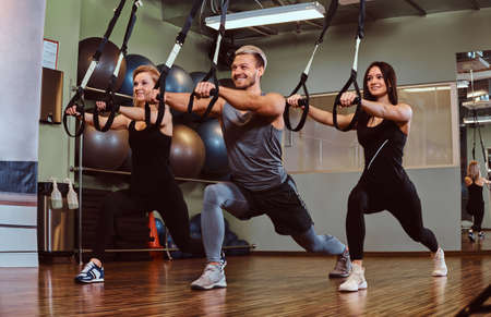 Group of people exercising with suspension straps in fitness club.