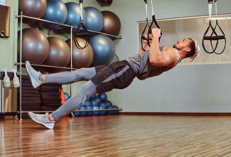 Handsome man in sportswear exercising with suspension straps in a fitness club.