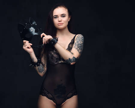 Sexy woman wearing black lingerie in BDSM cat leather mask and accessories posing on dark background.の写真素材