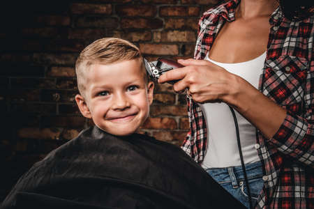 Cute preschooler boy getting haircut. Children hairdresser with trimmer is cutting little boy in a room with loft interior.の写真素材