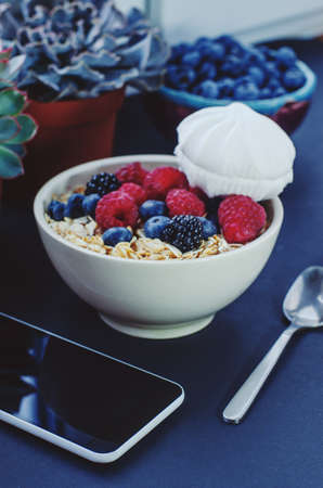 Healthy breakfast. White plate with oatmeal strewn and different berries on a blue background. Summer harvest.の写真素材