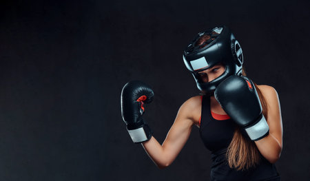 Sportive woman in sportswear wearing a protective helmet and boxing gloves, training in gym....