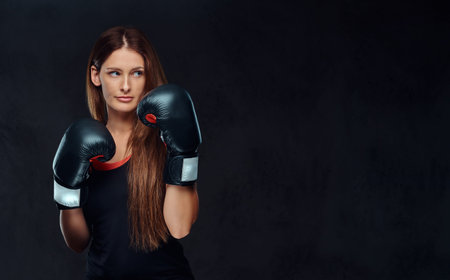 Sportive woman dressed in sportswear wearing boxing gloves posing in a studio. Isolated on a dark textured background.の写真素材