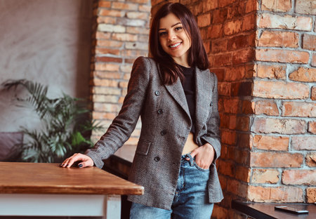 Smiling sensual brunette woman dressed in trendy clothes posing in a room with loft interior,...