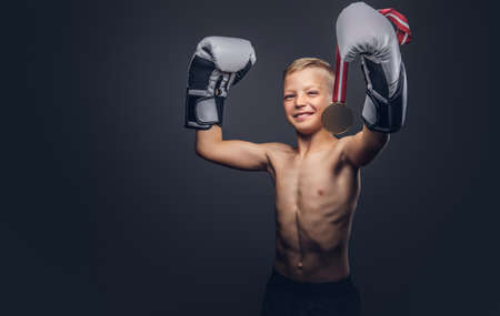 Joyful shirtless boy boxer in boxing gloves holds a golden medal posing in a studio.の写真素材
