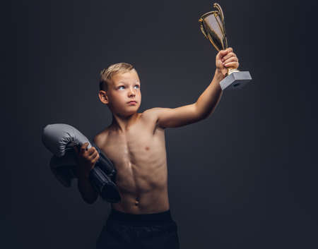 Young shirtless boy holds boxer gloves and the winners cup.の写真素材