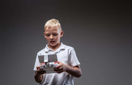 Handsome little boy boxer with blonde hair dressed in a white t-shirt holds a quadcopter control remote.の写真素材