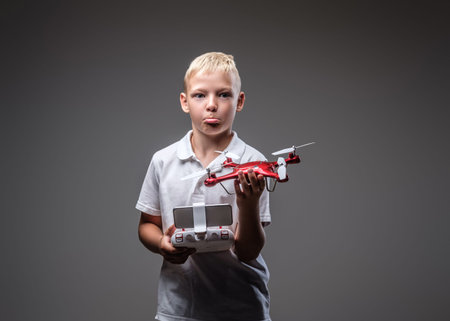 Funny boy boxer with blonde hair dressed in a white t-shirt holds a quadcopter and control remote.