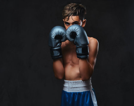 Portrait of a handsome shirtless young boxer wearing gloves. Isolated on a dark background.