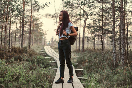 Full body portrait of a tourist girl standing on wooden footpath in a beautiful forest.の写真素材