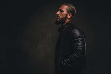 Profile of a fashionable bearded male in a black jacket. Isolated on dark textured background.の写真素材