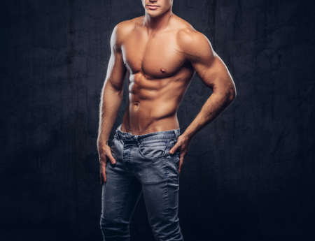 Cropped photo of a sporty guy with muscular body in jeans posing in studio.の写真素材