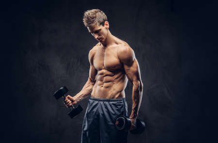 Handsome shirtless man with stylish hair and muscular ectomorph body doing the exercises with dumbbells.の写真素材