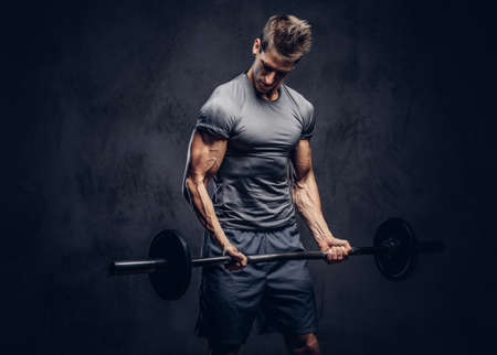 Handsome sportsman with stylish hair dressed in a sportswear doing the exercises with the barbell.の写真素材