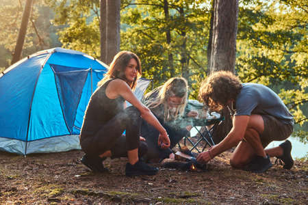 Three friends hiking in the forest and try to light a fire at camp.の写真素材