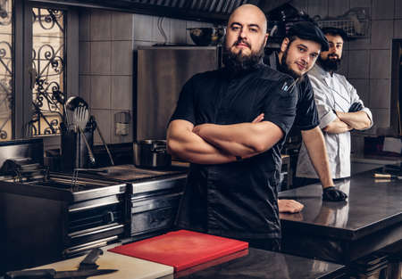 Team of professional bearded cooks dressed in uniforms standing in kitchen.の写真素材