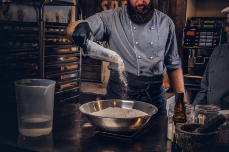 Chef pours the flour into a bowl. Chef teaching his assistant to bake the bread in the bakery.の写真素材