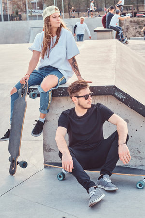 Young stylish couple of a trendy dressed skaters relaxing at a skatepark.の写真素材