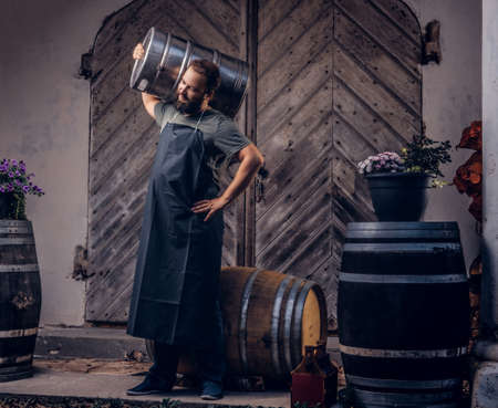 Brewer in apron holds barrel with craft beer at brewery factory.の写真素材