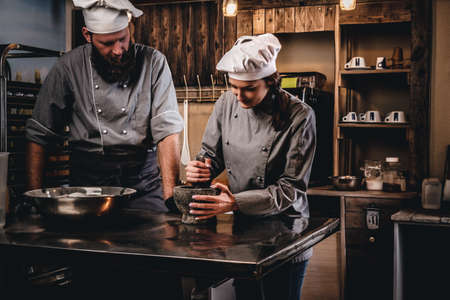 Assistant cook grinds sesame seeds in a mortar for cooking bread. Chef teaching his assistant to bake the bread in the bakery.の写真素材