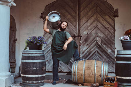 Brewer in apron holds barrel with craft beer at brewery factory.の写真素材