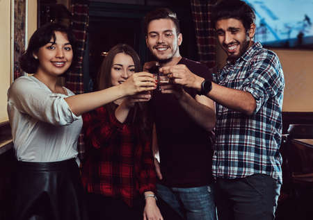 Group of happy multiracial friends making a toast with vodka while standing at bar or pub.の写真素材