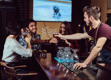 Young multiracial friends in bar. barman giving glass of beer to customer in pub.の写真素材