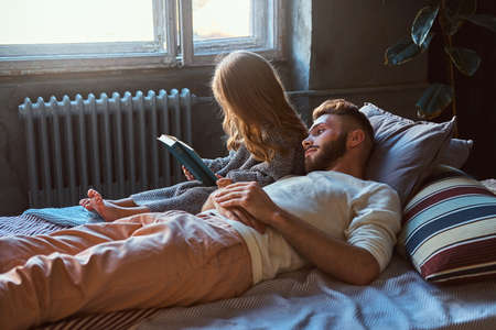 Handsome young father and daughter reading storybook together while lying on bed.の写真素材