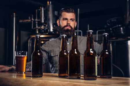 Photo with craft beer bottles on the foreground and bearded male drinking on the background.の写真素材