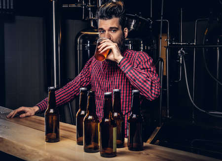Hipster male with stylish beard and hair drinking beer sitting at the bar counter in indie brewery.の写真素材