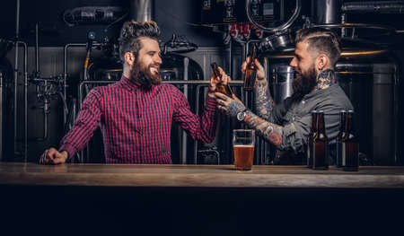 Two stylish bearded hipsters friends drinking beer together at indie brewery.の写真素材