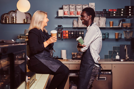 Two young multiracial baristas relaxing after work laughing and talking together at the trendy...