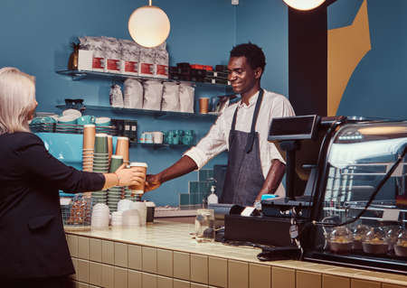 African American barista giving cup of coffee to his female client at the trendy coffee shop.の写真素材