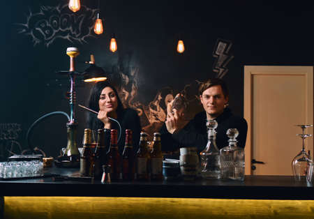 Brunette girl with hookah and barmen at the counter in a nightclub, looking at camera.の写真素材