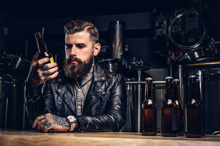 Stylish bearded biker dressed black leather jacket sitting at bar counter in indie brewery.の写真素材