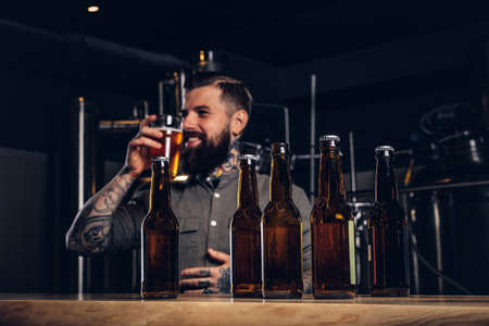 Photo with craft beer bottles on the foreground and bearded male drinking on the background.の写真素材