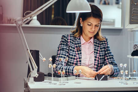 Woman seller packs precious earrings in a box for her client in a luxury jewelry store.