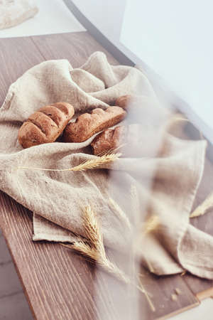 Freshly baked buns and spikelets of wheat lying on a linen cloth.の写真素材