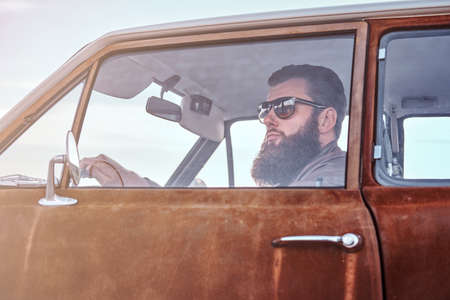 Bearded male dressed in brown leather jacket driving a retro car.の写真素材
